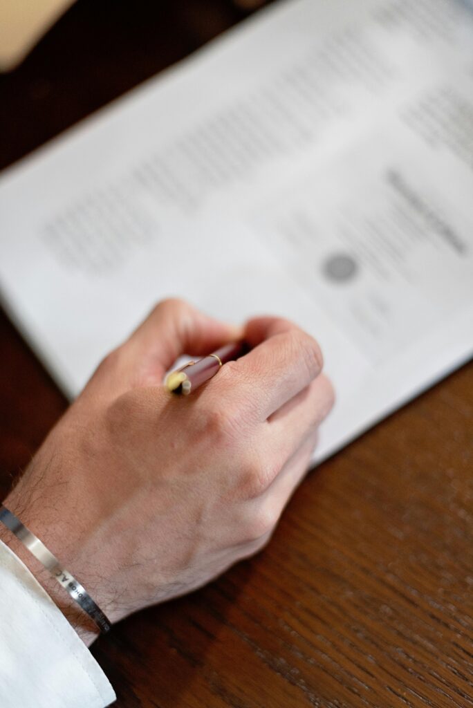 Complete Guide to Document Attestation in the UAE (2026) A close-up image of a hand holding a pen signing a formal document on a wooden table.